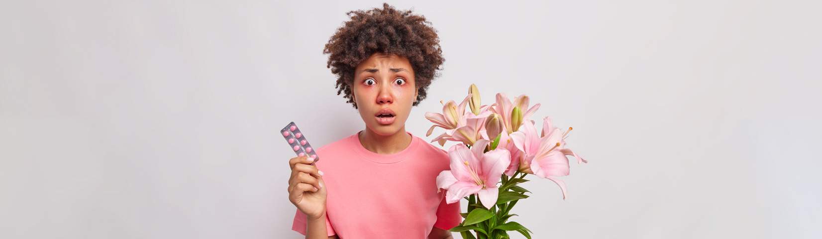 woman with curly hair holds bouquet lily flowers has allergic reaction pollen holds medicaments cure symptoms disease wears pink t shirt isolated whitee